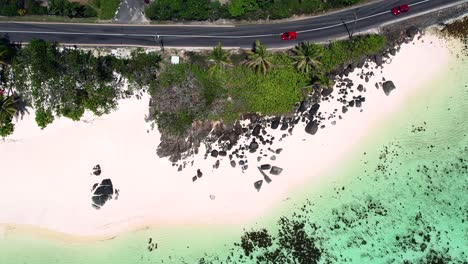 mahe seychelles drone shot of car passing on the road near the beach, palm tees and granite rocks can be seen, white sandy beach and turquoise water