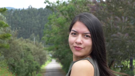 pretty hispanic, latino female model poses turning to the camera and smiling, in nature