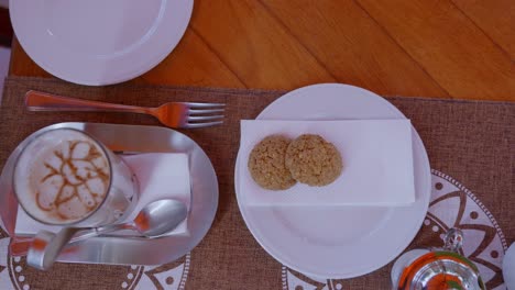 person picking up one cookie from plate near coffee on wooden table