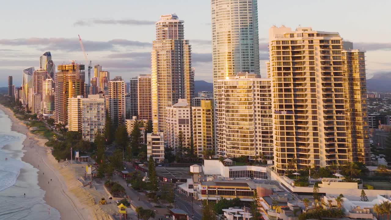 Aerial footage captures Gold Coast's skyline at sunset, highlighting tall buildings and the adjacent beach with warm lighting