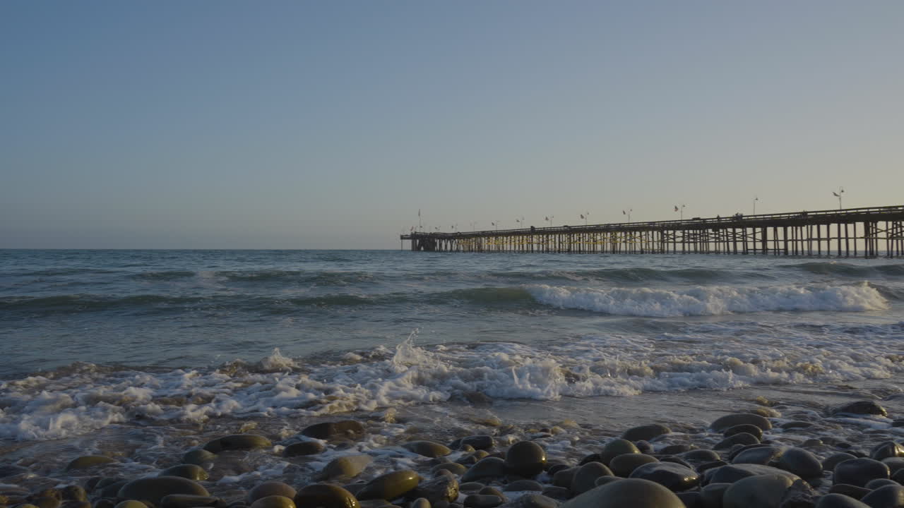 Panning shot of waves crashing along the shores of Ventura Beach at sunset with the Ventura Pier in the background located in Southern California