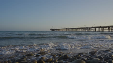 在南加州的ventura pier在背景下,在日落时沿着ventura beach的海岸崩<unk>的波浪.