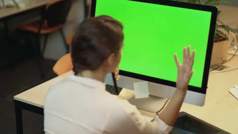 Young-woman-working-on-computer-with-green-screen-in-office