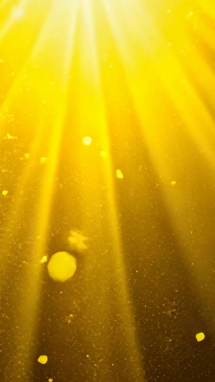 Vertical video: Intensifying glow spawning golden light beams in studio, with drifting specks