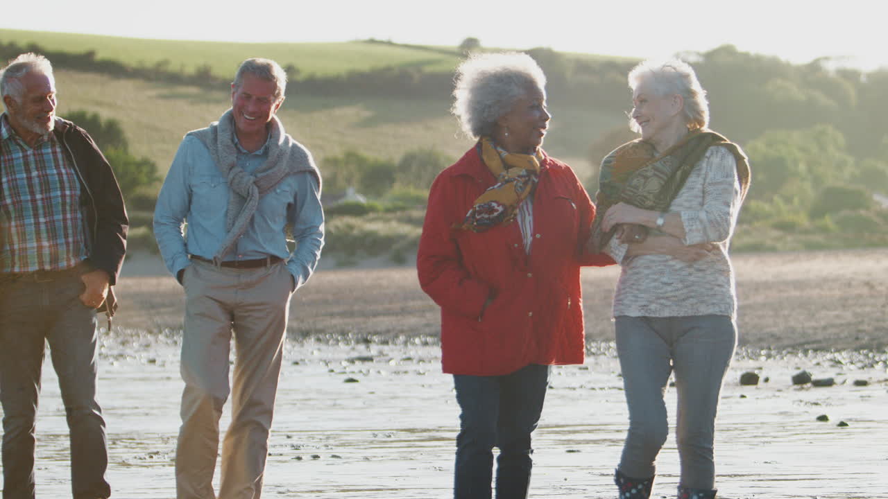 grupo de amigos mayores caminando a lo largo de la costa de la playa de otoño