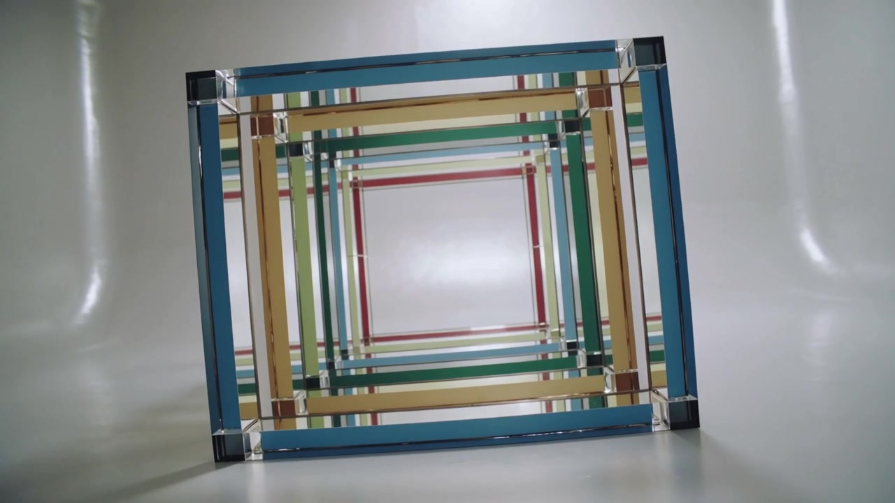 Carrello telecamera che parte rivelando una scultura di quadrati annidati multicolore su uno sfondo chiaro, centrando l'inquadratura.