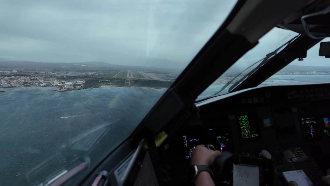 immersive pilot’s perspective through the windshield of a jet airplane flying through a thunderstorm in the final approach to Palma Airport, wiyh a view of pilot’s hand on the controls.