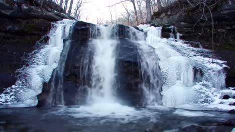 a stunning view of a frozen waterfall cascading over rocky terrain surrounded by bare trees, showcasing nature's icy beauty in a serene winter wonderland