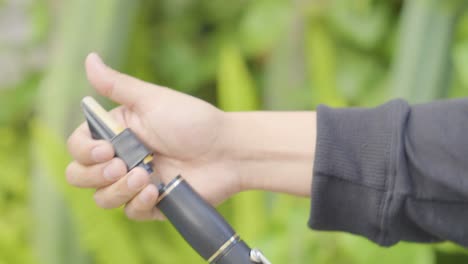 cerca de la mano de un hombre girando y pegando una pieza de boca a un clarinete afuera con fondo borroso verde