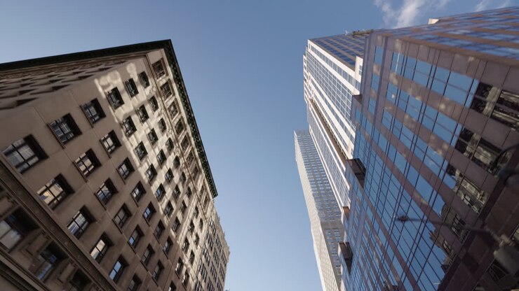 low angle view of manhattan skyscrapers with american flag and mix of modern and classic facades against clear blue sky
