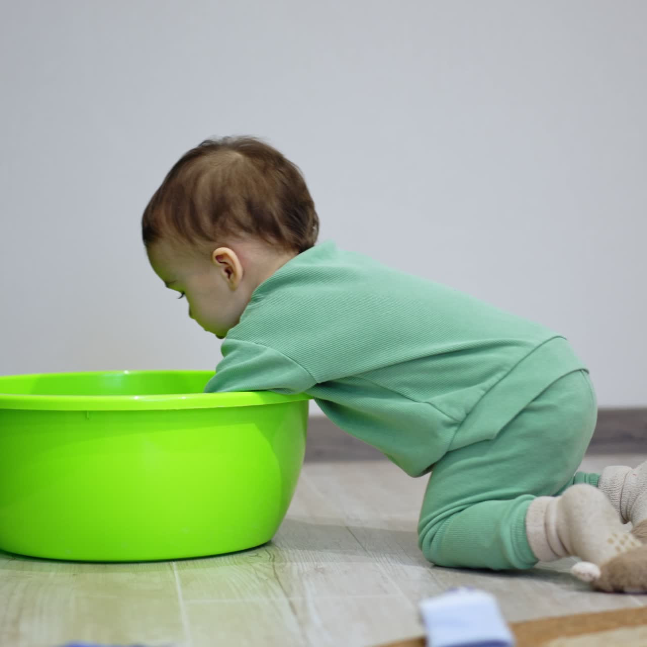 Baby boy approaches the washbowl crawling on his knees. Kid puts a yellow ball inside the tub and tries to get there himself but fails