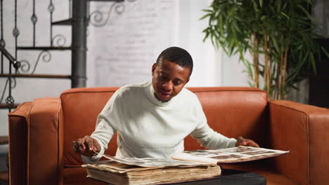 African-American-man-looks-at-antique-family-photos-on-sofa