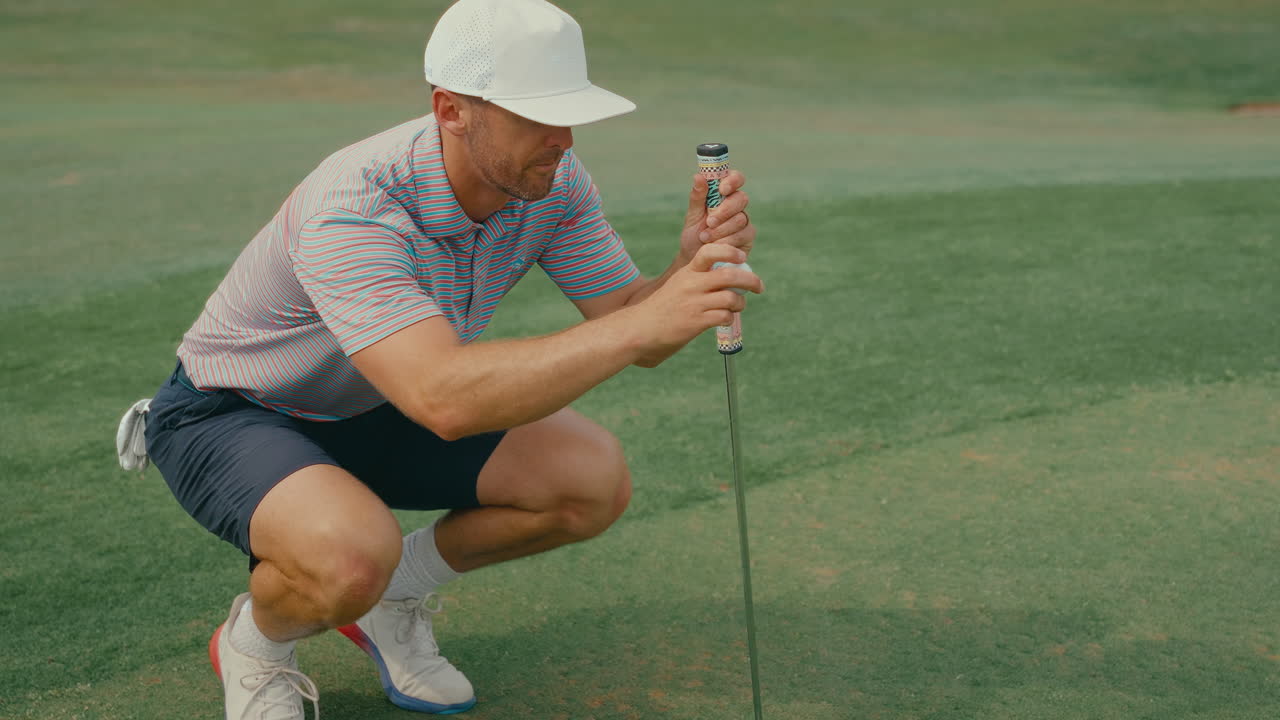 Male golfer uses AimPoint technique, holding fingers in air to read green slope before putting. Focused pre-shot golf routine on a sunny course.