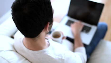 hombre bebiendo un café blanco mientras usa su portátil
