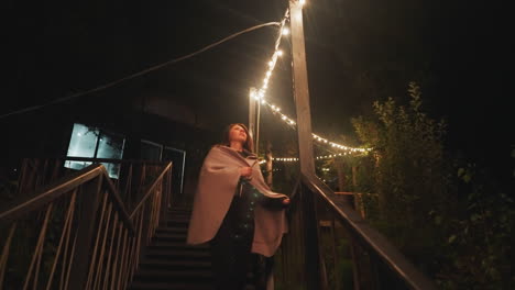 contemplative lady descends stairs in backyard. pensive woman strolls through well-lit private spaces of home late in evening. bright illumination