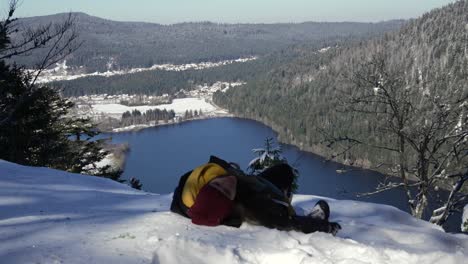 Excursionista-Caucásica-Descansando-En-La-Nieve-En-La-Cima-De-Una-Montaña-Con-Vistas-Al-Lago-Longemer,-Vosgos,-Francia