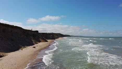 Flying-Over-Coastline-Baltic-Sea-Ulmale-Seashore-Bluffs-Near-Pavilosta,-Latvia-and-Landslides-With-an-Overgrown,-Rippling-Cave-dotted-Cliff-and-Pebbles