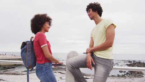 una joven pareja afroamericana sonriendo mientras hablan entre sí en el paseo cerca de la playa