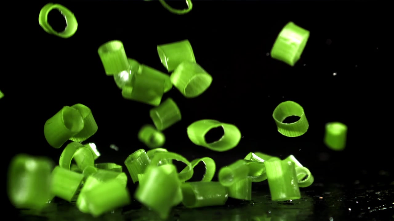 Chopped Green Onions Falling in Slow Motion on Black Background