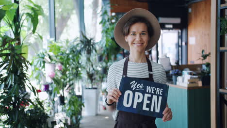 woman in a floral shop holding an open sign