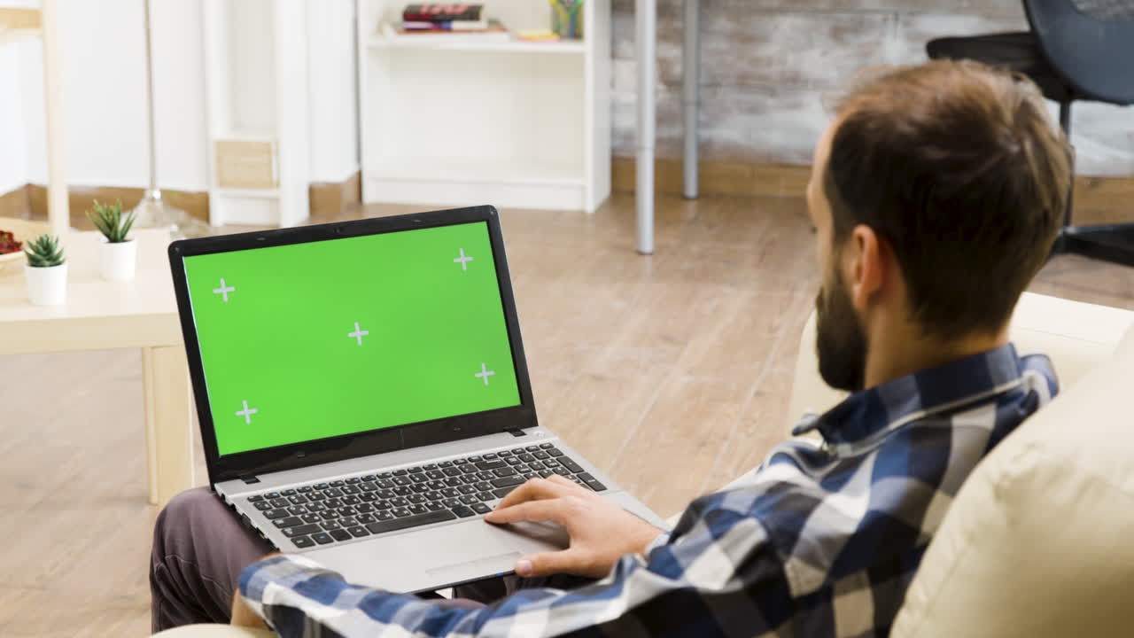 Man working on laptop with green screen at home