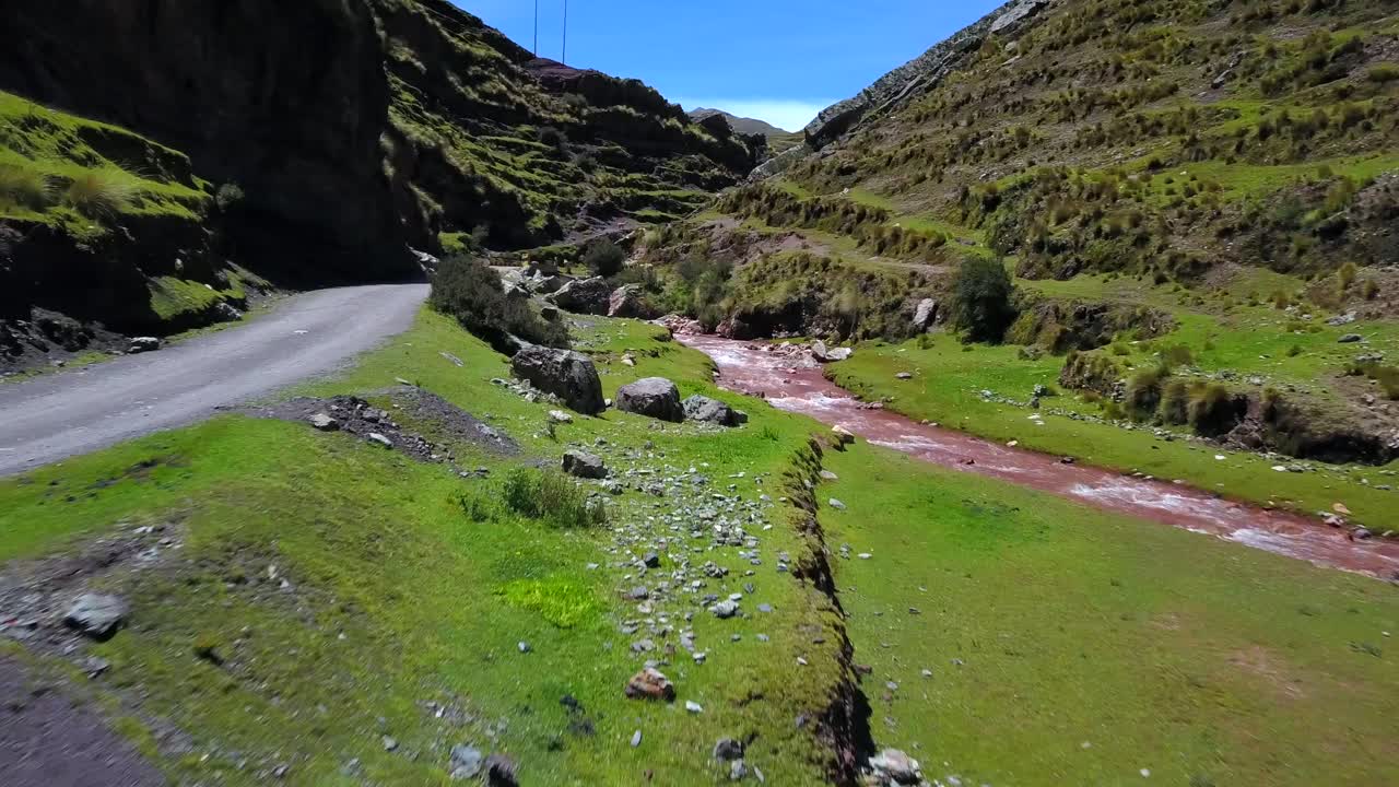 Aerial, drone shot of a road and the Pukamayu Red River, on a sunny day, in Cusco, Peru, South America