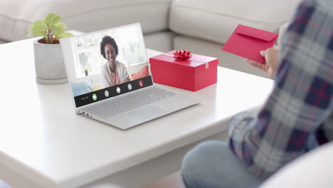 Caucasian-man-holding-envelope-and-talking-with-african-american-woman-on-laptop-screen