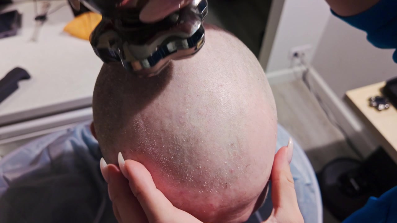 Woman carefully shaving male scalp with electric clipper during grooming session