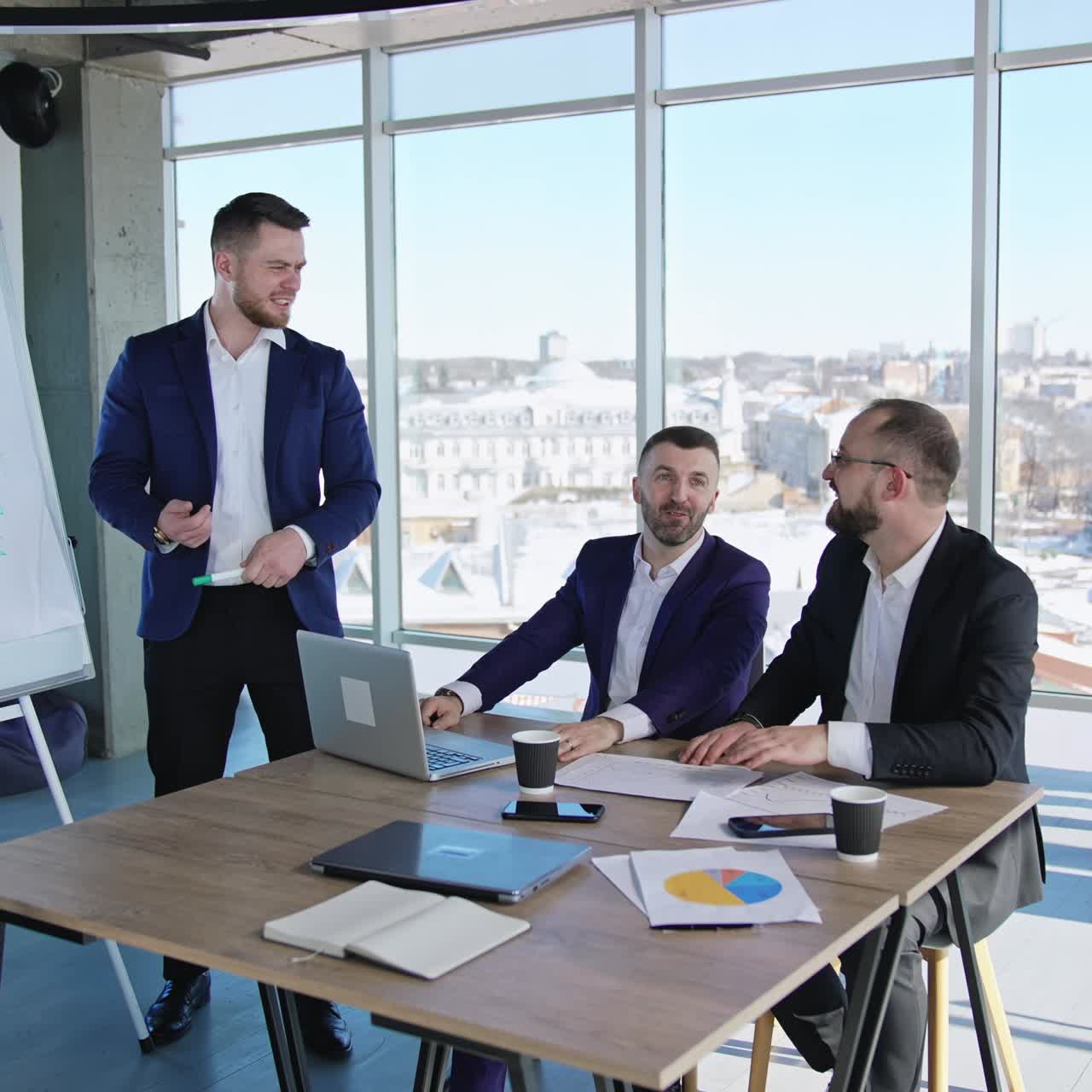 Business people collaborating in the office. Male team at the table working at the foreground. Women colleagues near the window at the backdrop