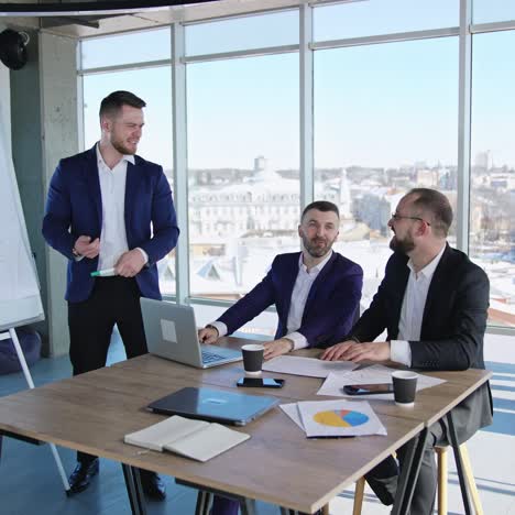business people collaborating in the office. male team at the table working at the foreground. women colleagues near the window at the backdrop
