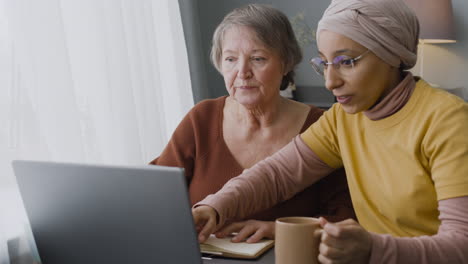 arabic woman teaching an elderly woman to use a laptop at home 2