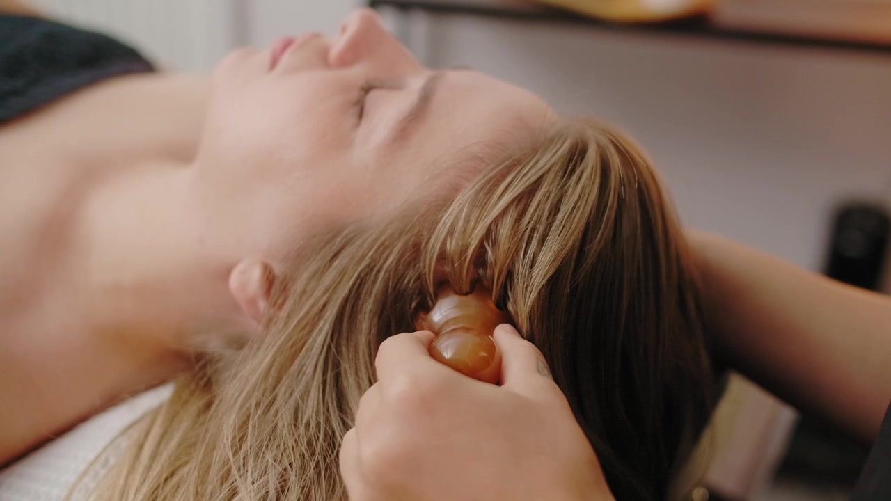 Terapista professionista che esegue un massaggio al cuoio capelluto con uno strumento Gua Sha
