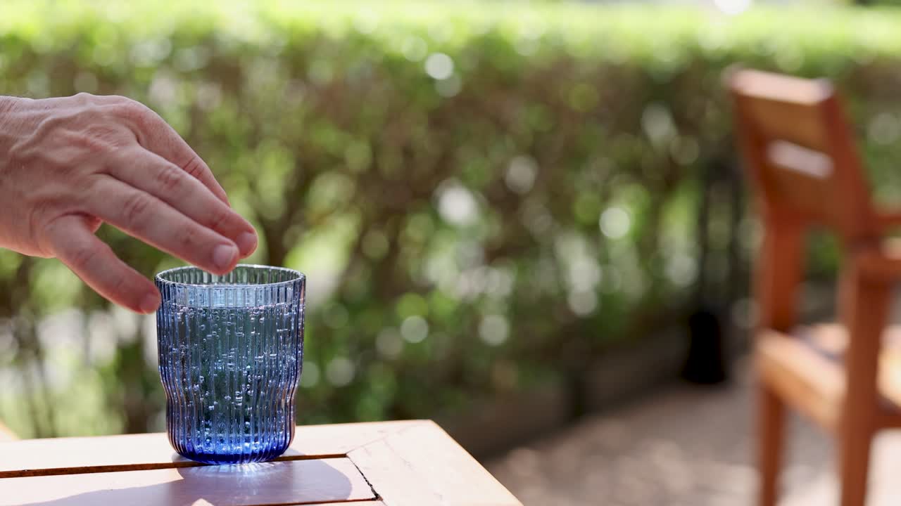 una mano exprime un limón en un vaso azul de refresco en una mesa al aire libre soleada