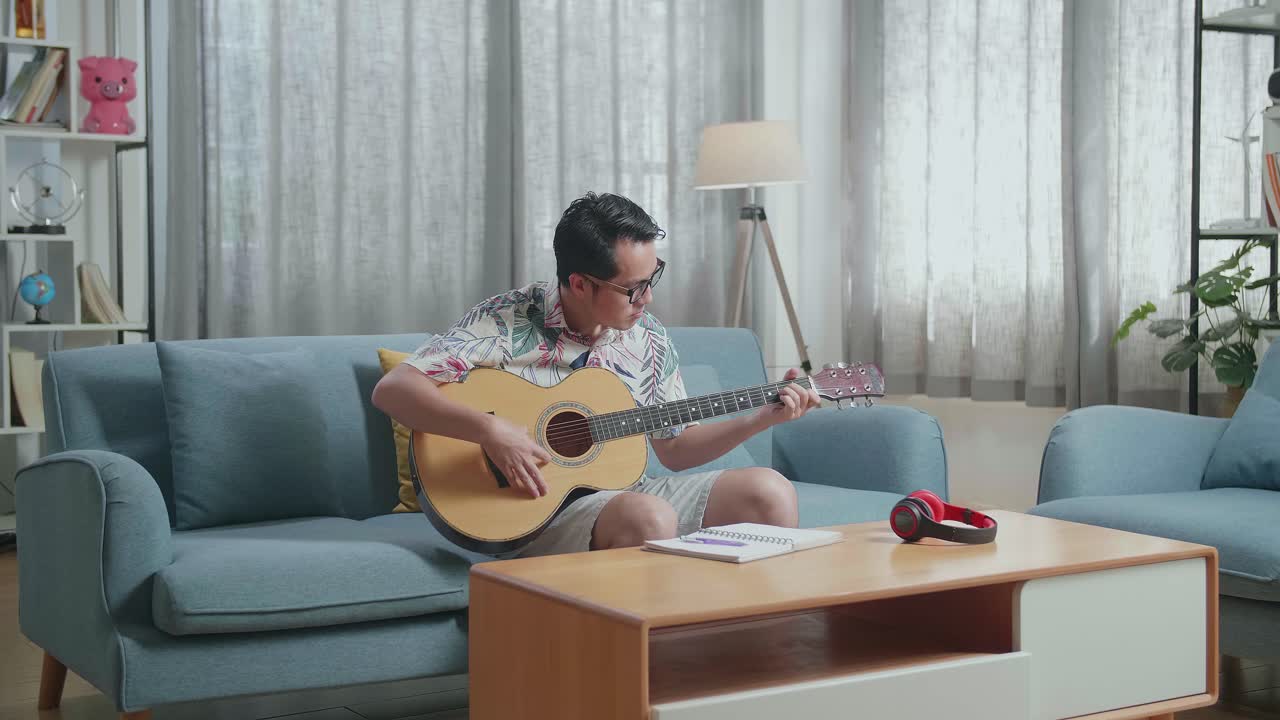 노트북을 들고 집에서 기타를 연주하는 아시아인 작곡가