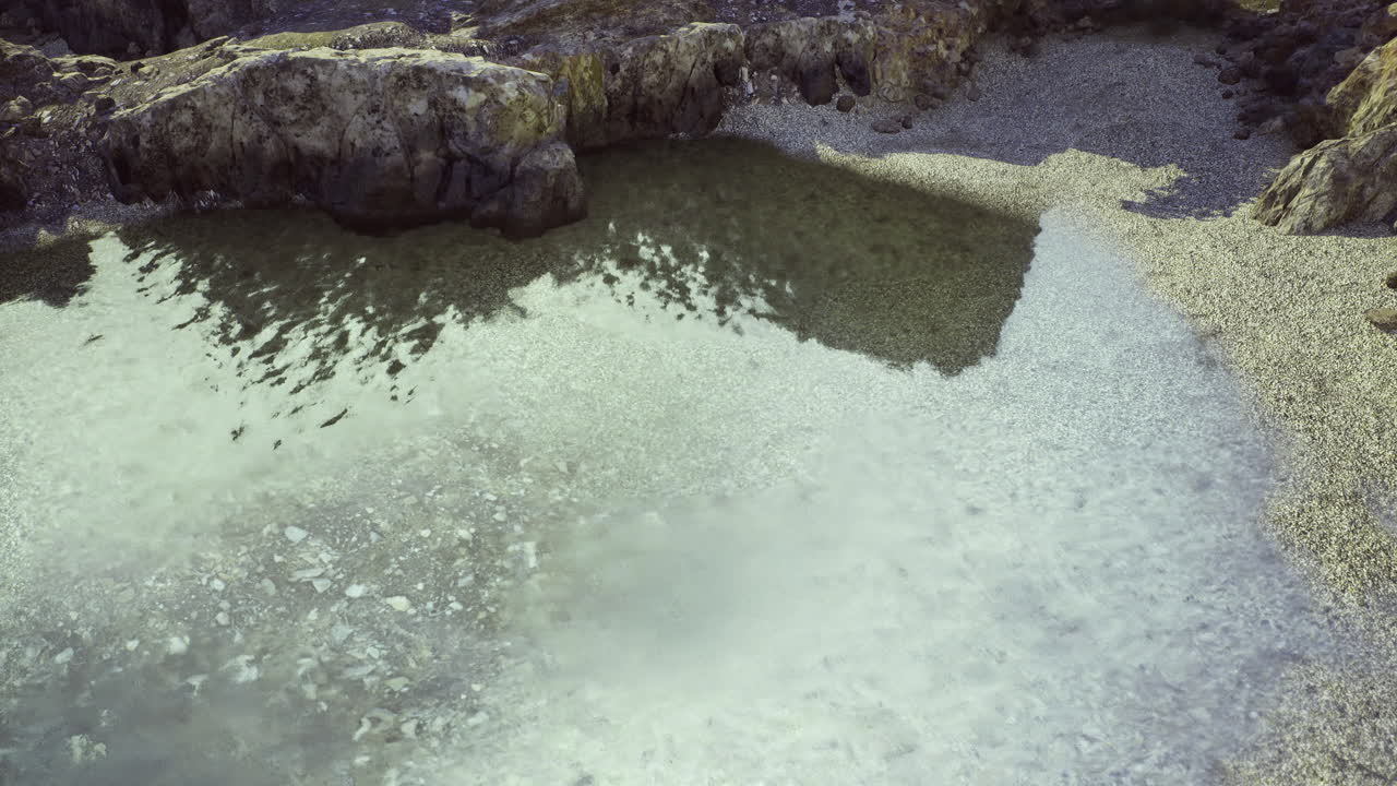 Rocky shoreline with calm waters reflecting the sky near a beach area