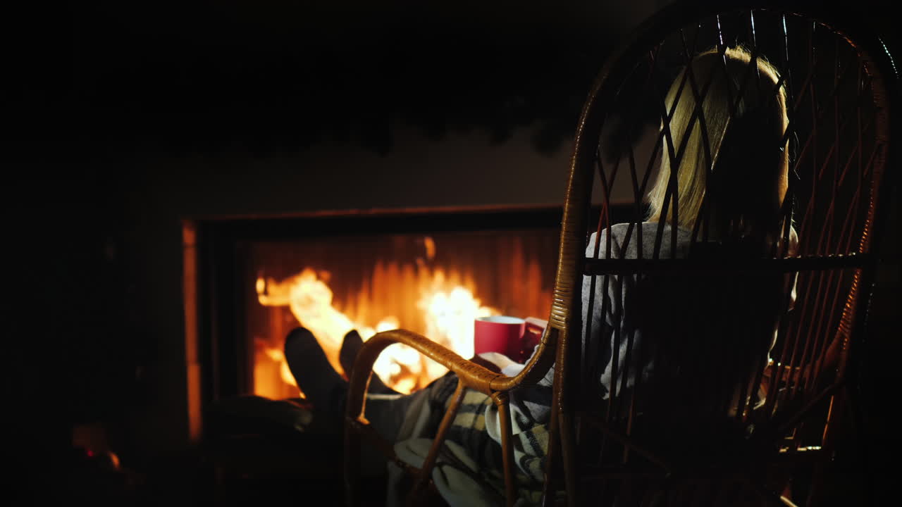 한 젊은 여성이 벽난로 겨울 탈출 컨셉으로 차 한 잔과 함께 휴식을 취하고 있습니다.