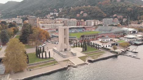 monumento de guerra de piedra en forma de torre con el estadio giuseppe sinigaglia en el fondo, como, lombardía, italia