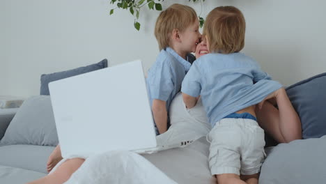 mom is sitting on the couch with a laptop. two children of boys sing and kiss their mother. happy family, loving children