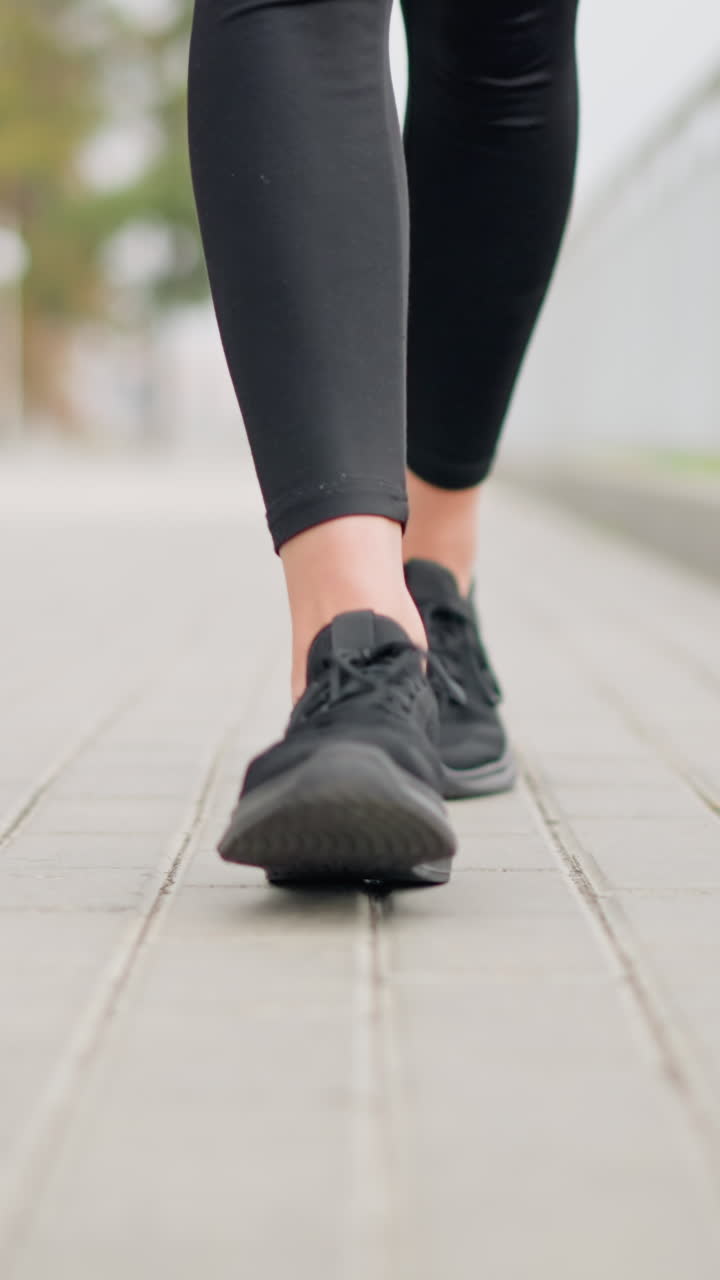 Close-up of fair woman leg in black shoes walking confidently on smooth pavement with iron fence in background, focusing on shoes and walking style in serene urban environment