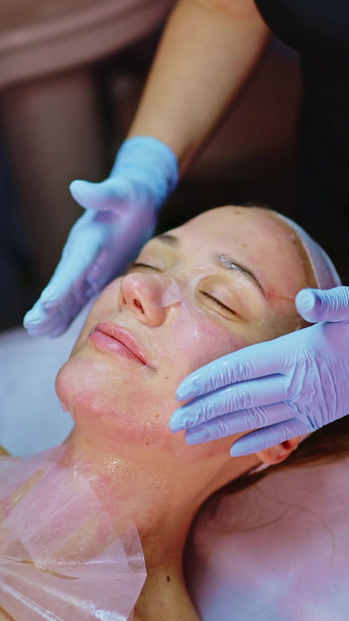 Una donna riceve un trattamento facciale in un centro estetico; le mani dell'estetista applicano il prodotto sulla sua pelle durante una seduta spa serale.