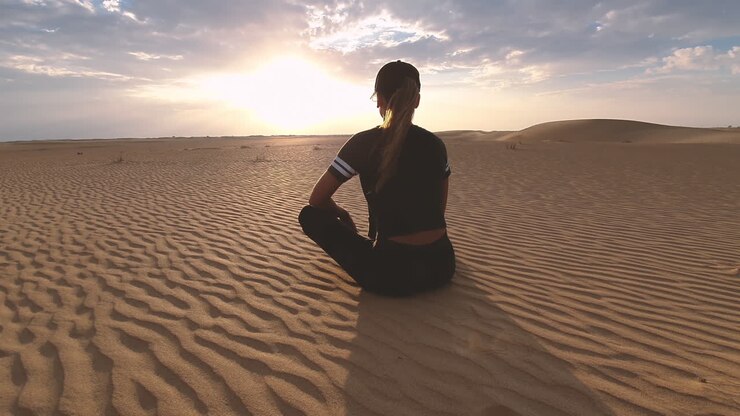Mulher meditando no deserto ao pôr-do-sol
