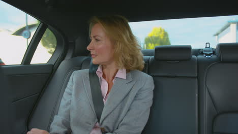 mature businesswoman sitting in back seat of taxi or car working on laptop