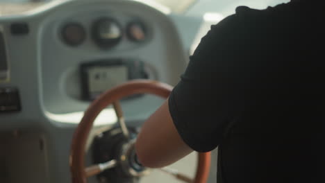 skilled skipper controls modern yacht with helm in cockpit closeup. man in black t-shirt sails motor boat on sunny day. capitain on shift at dashboard