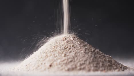 Video-of-close-up-of-sand-grains-pouring-into-heap-and-copy-space-on-black-background