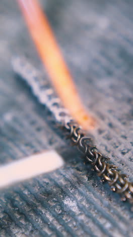 cu: professional jeweler applies material by flame heating to decorative chain with brush on asbestos sheet close view