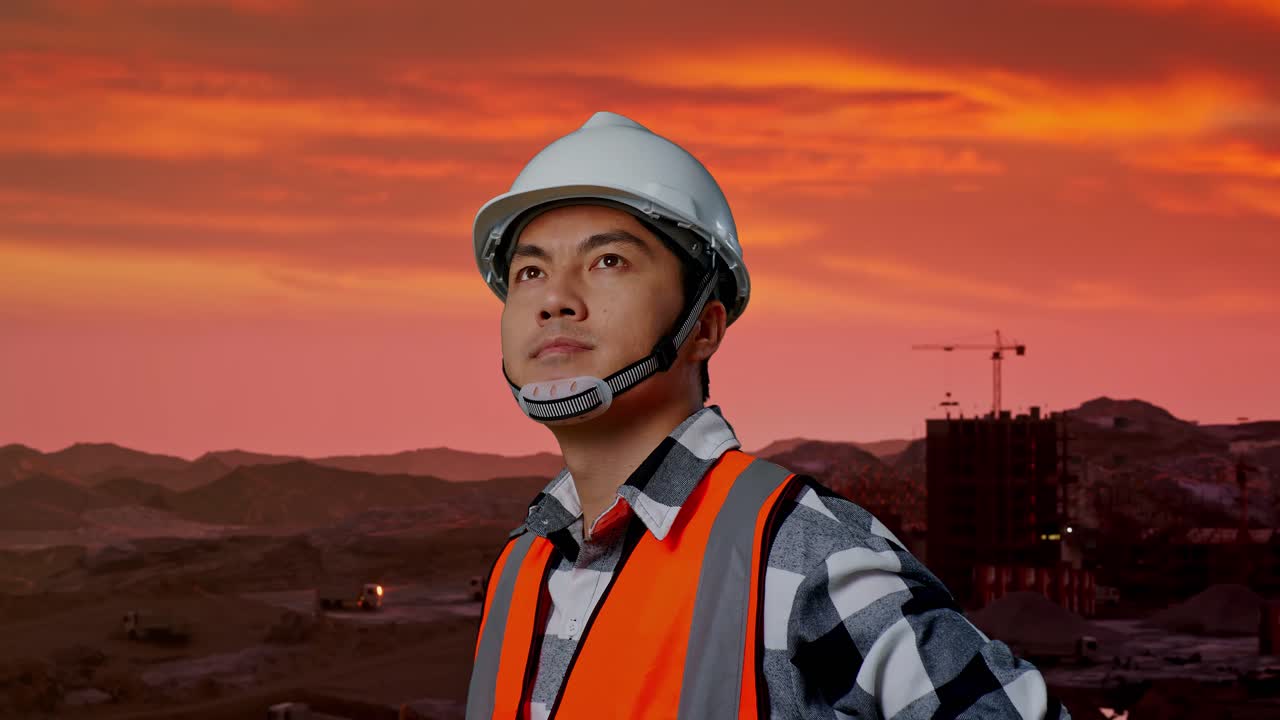 안전 헬을 착용 한 아시아 남성 엔지니어의 가까운 측면 뷰는 건설 현장에서 팔을 들고 서있는 동안 주위를 둘러보고 있습니다.