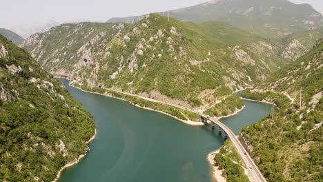 aerial view over part of the neretva river with a bridge over a tributary in bosnia with the road at the foot of the mountains