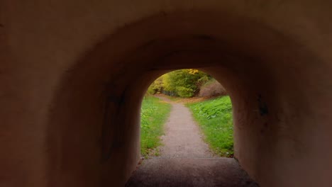 drone passes through the middle of three tunnels located under a bridge on the other side offers a view of the forest and the city wall of an old historic town