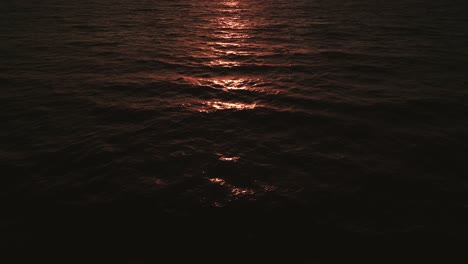 Aerial-flight-over-the-open-sea-ocean-by-sunset-with-the-red-and-orange-sunlight-reflecting-on-the-water-and-waves-in-slow-motion