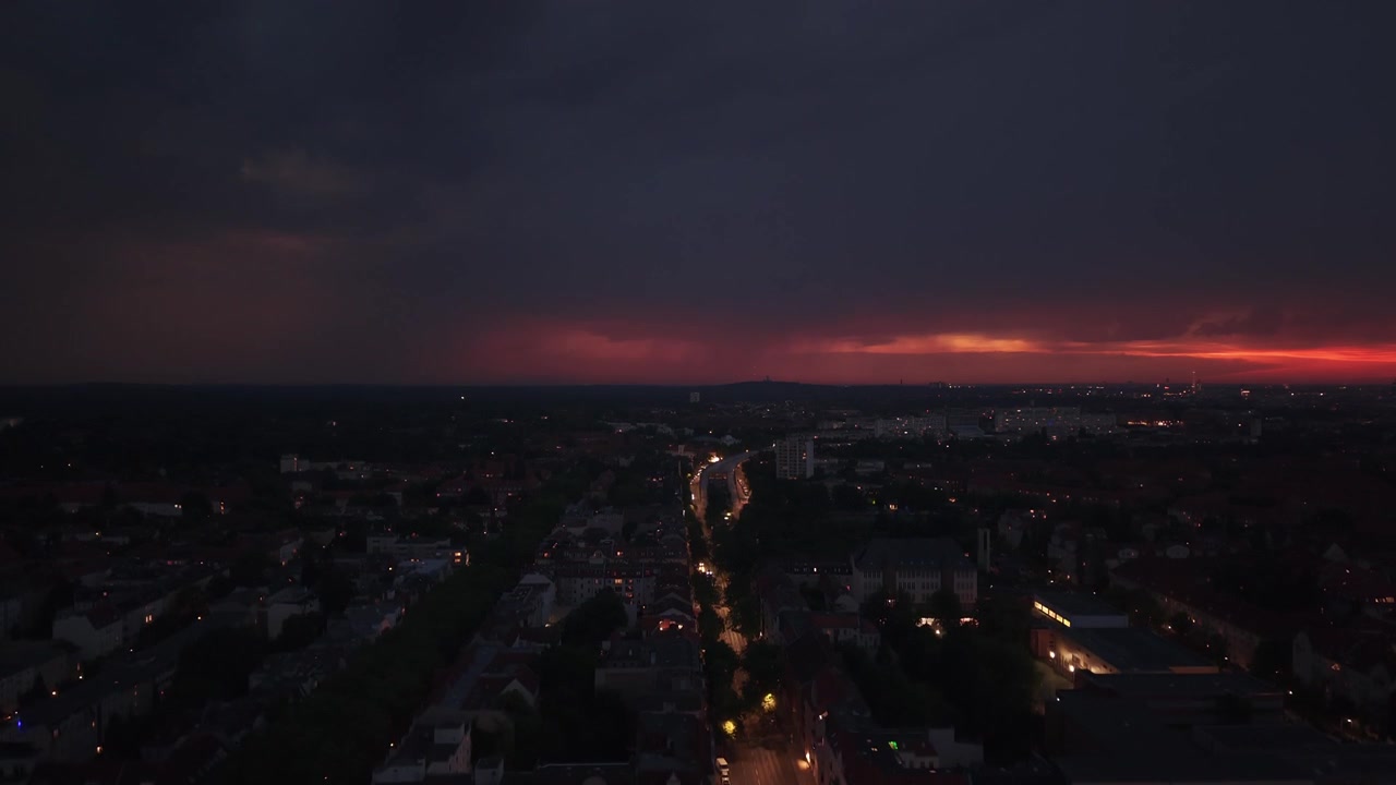 Město s viditelným úderem blesku proti bouřkové obloze, osvětlující městskou krajinu v noci. Magický stoupající panoramatický záběr dronu.